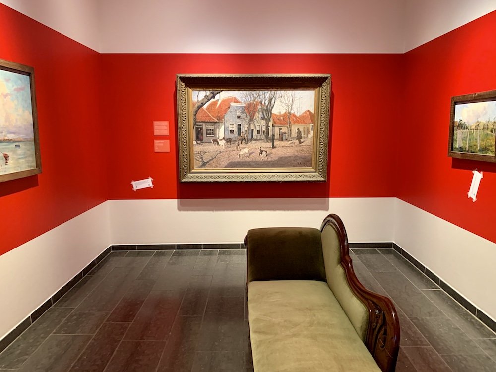 red walls of a museum room with a painting of a norewgian street scene