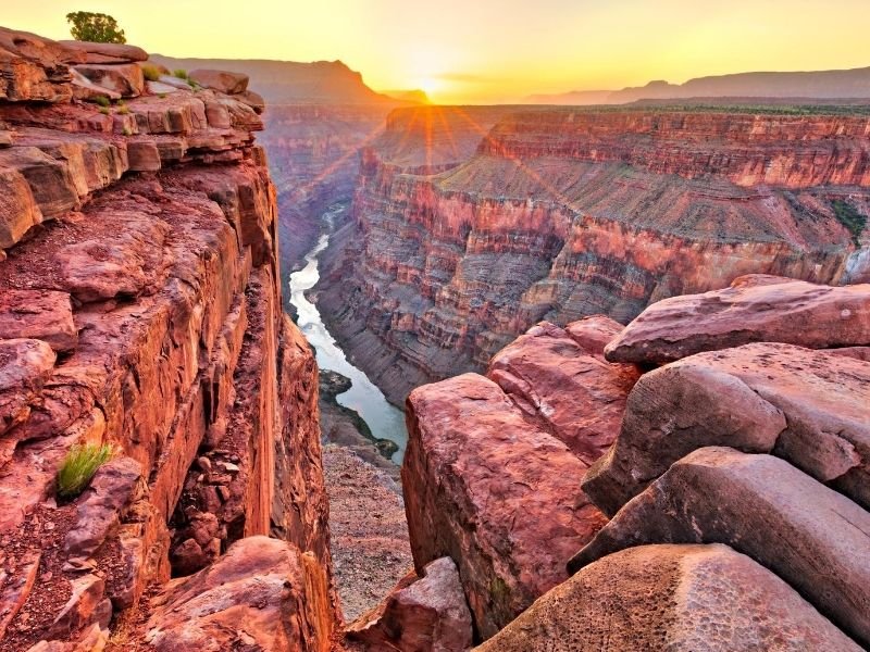 view of the Grand Canyon at sunrise with the sun cresting over the valley and river with brilliant red and orange colors