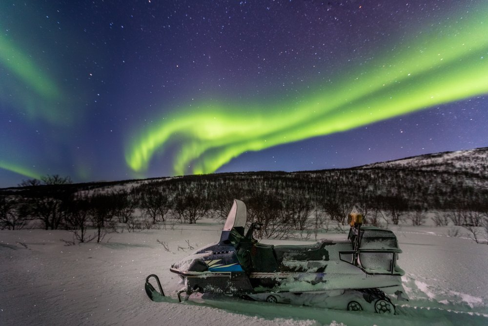 snowmobile with the aurora behind it during the night in tromso with wild lights in the sky