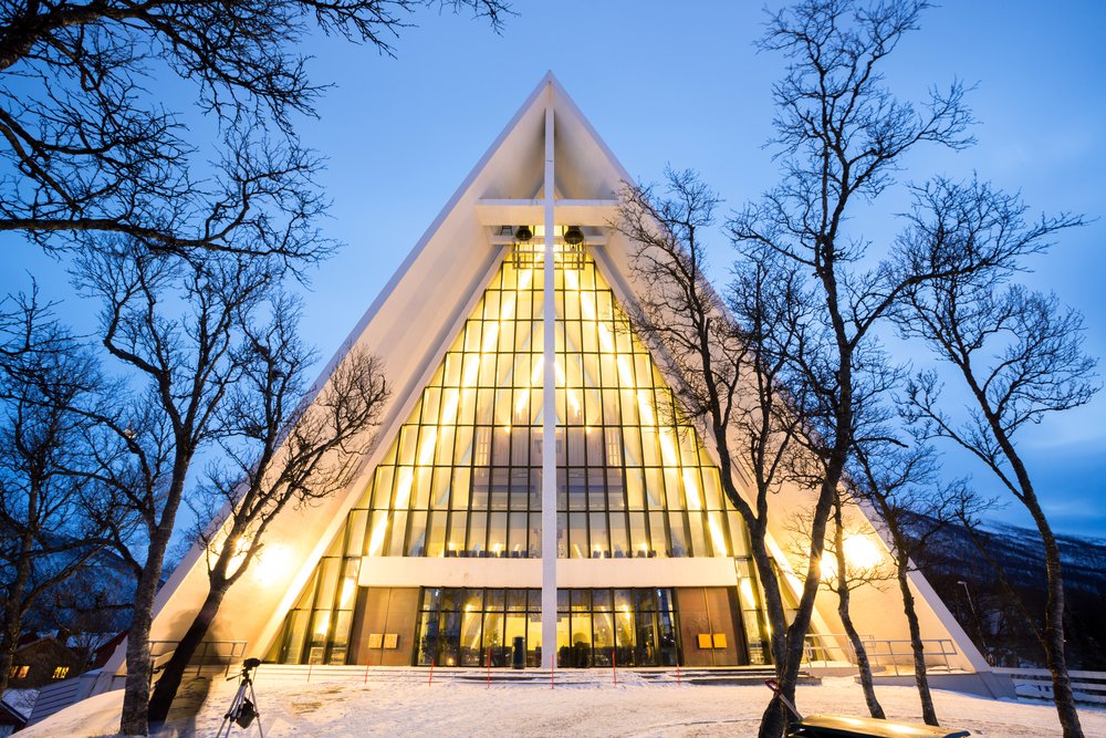 lights on in the triangular shaped arctic cathedral in downtown tromso with pale blue sky as the sun has just set in the city.