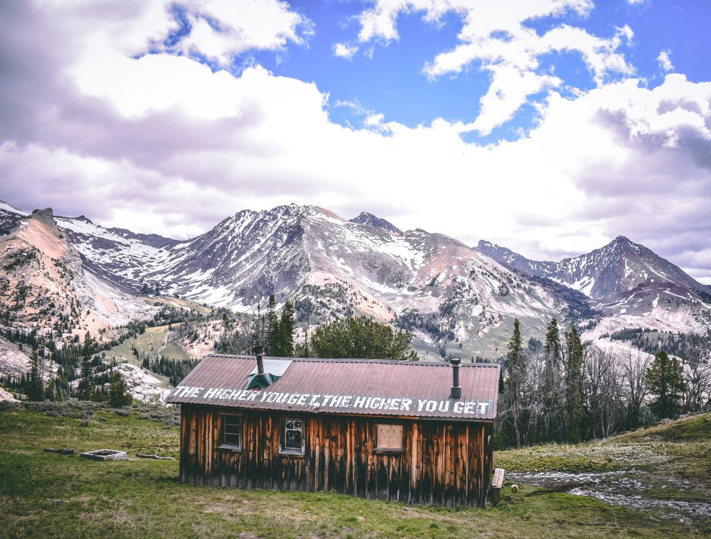 A building which reads "the higher you get the higher you get" on the roof top, a popular site near Ketchum in the Sun Valley, with mountains and trees in the distance.