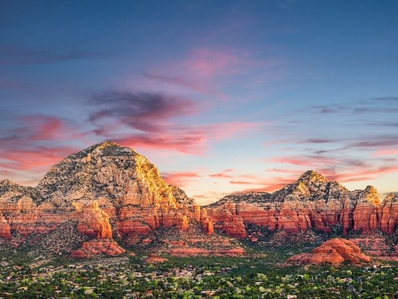 A colorful sunrise over the red rock formations of Sedona and the trees in the valley