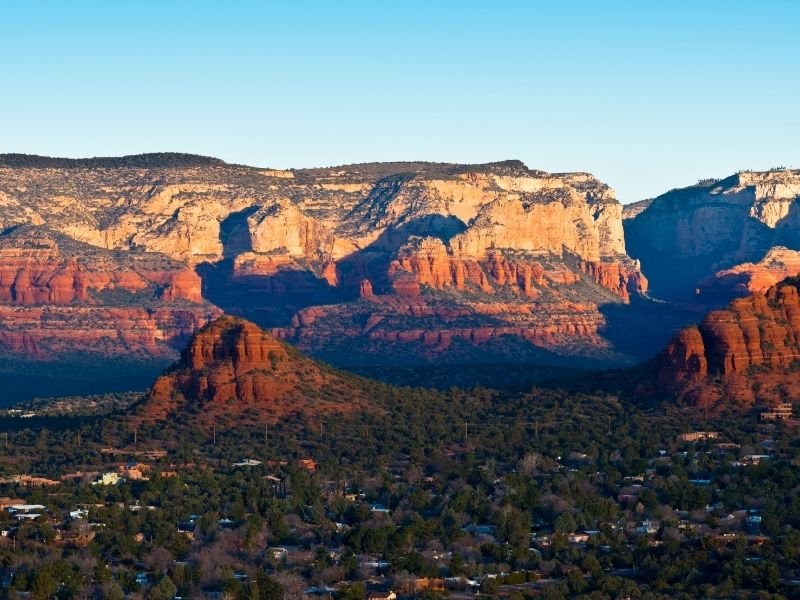 Sunrise over the red rock formations of Sedona with trees in the valley and shrubs below