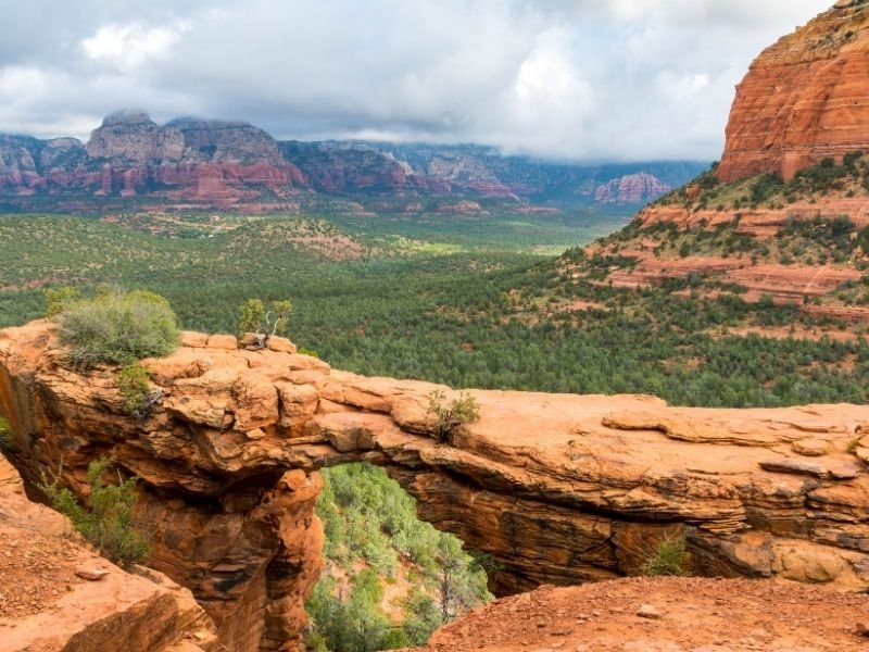 The natural bridge of Devil's Bridge in Sedona with red rocks and green trees all over the valley