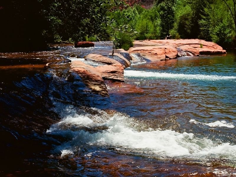 River next to red rocks with lush trees around it and lots of shade