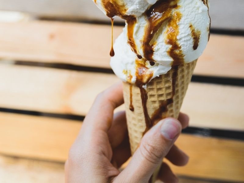 hand holding an ice cream cone dipping in caramel
