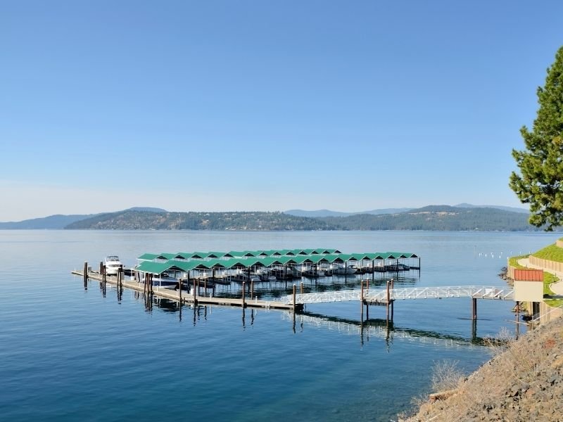 View of the boat houses on the lake at Couer D'alene: two rows of teal-roofed boat houses on a still lake with a dock.