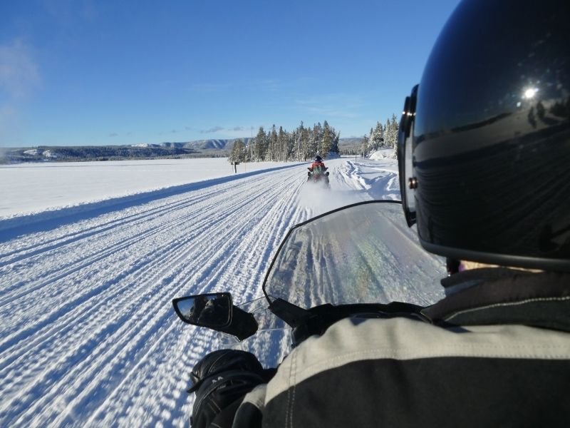 View from behind of a man on snowmobile with another snowmobile ahead on a sunny winter day.