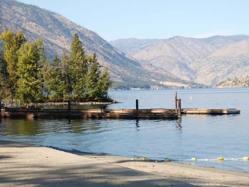 A view of Lake Chelan, a still lake with a small beachy area and dock, part of the hike in Stehekin.