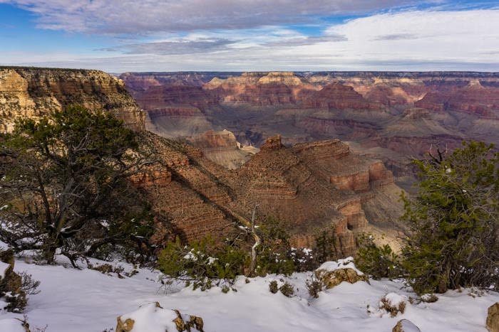 Snow on the edge of a canyon rim looking into the magnificent Grand Canyon on a partly cloudy sky day.