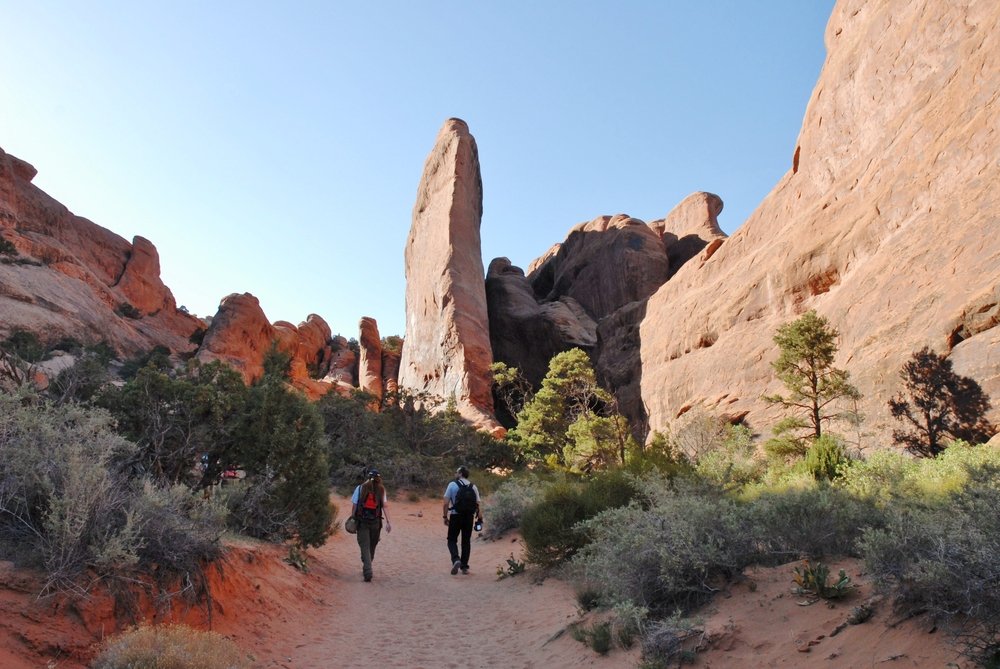 two hikers walking down a trail in the devils garden section of arches national park.