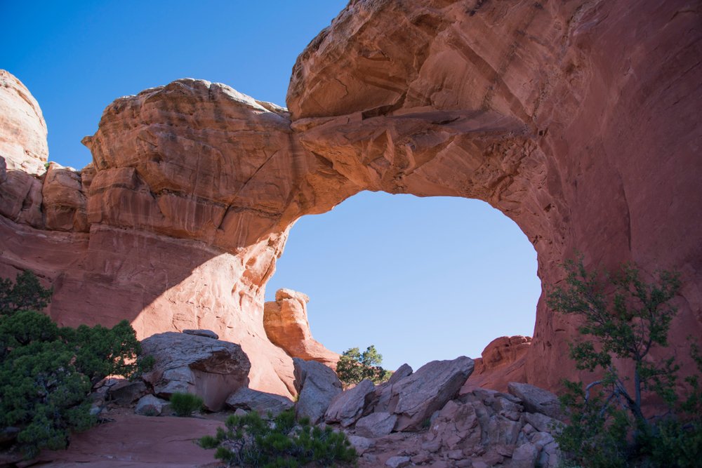 view of an arch that looks partly broken, with a small crack in the rock, seen at sunrise.