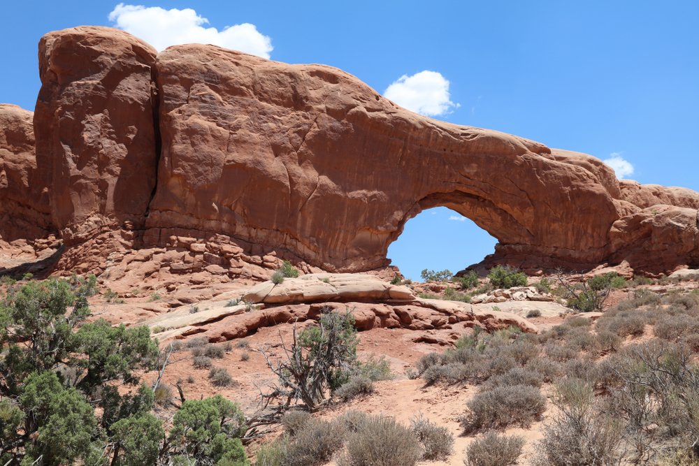 a giant rock with an arch showing blue sky behind it in arches national park