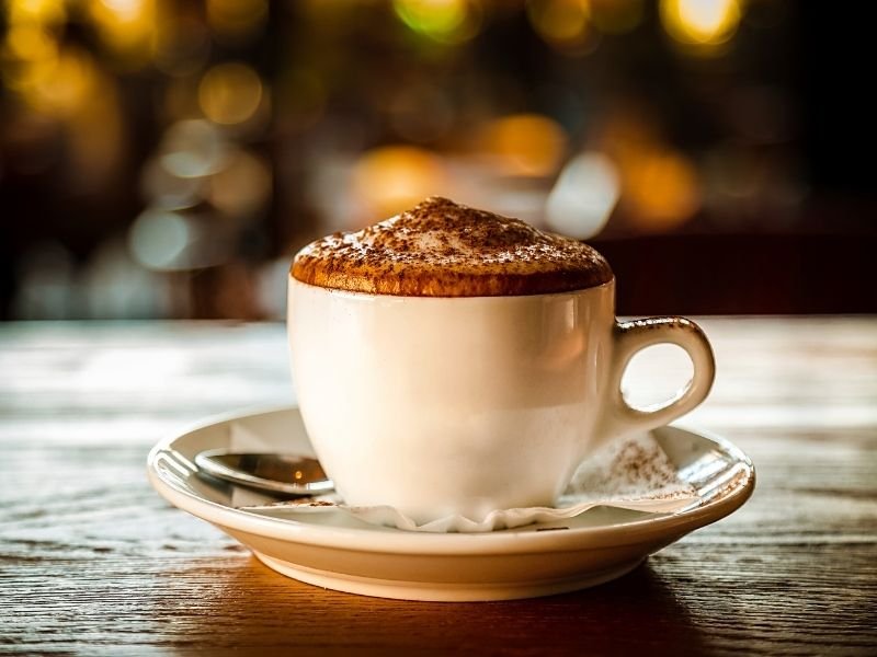 A perfect cappuccino with foam with chocolate on top, served on a wood table.