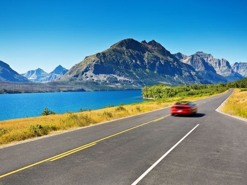 A blurry red car driving past a landscape road tripping in Montana's Glacier National Park