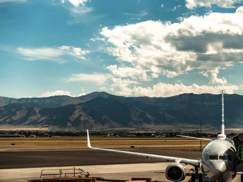 An airplane connected to a jet bridge with the mountains in the background as seen at a Montana airport