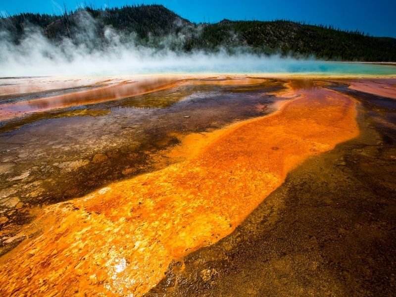 The orange and brown striations of Grand Prismatic Hot Spring in yellowstone national park with a steaming center that is bright turquoise blue.