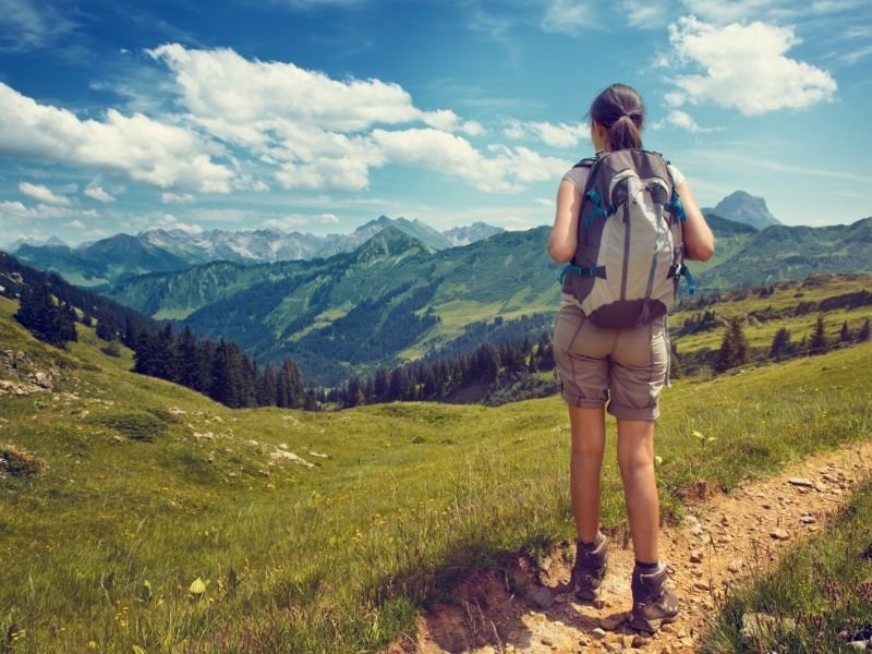 A woman in the Montana wilderness wearing shorts, hiking boots, and a day pack with her hair in a ponytail on a summery day.