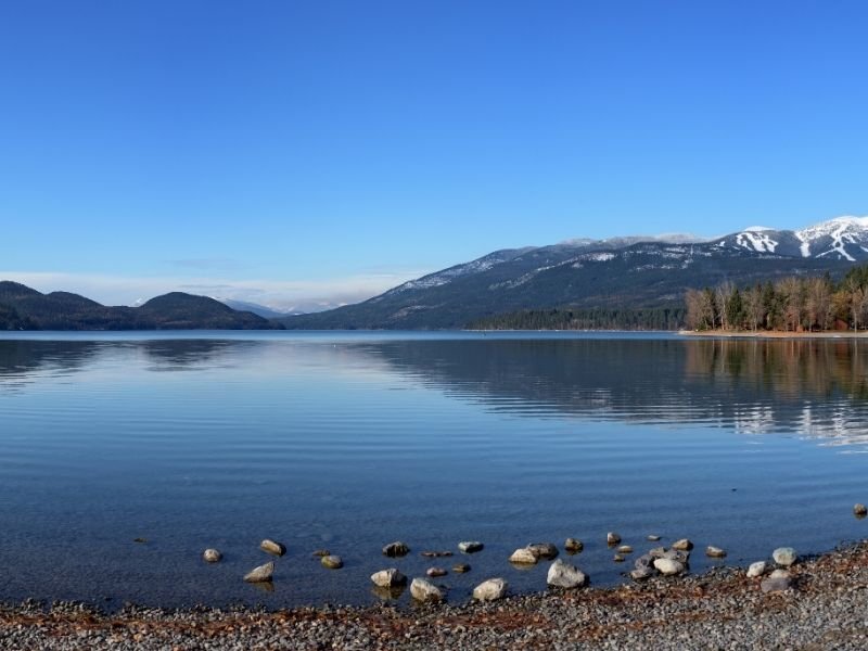 The shores of Lake Whitefish near Glacier National Park, a popular place to stay for easy park access. The lake is clear with some ripples and a slight reflection of the mountains.