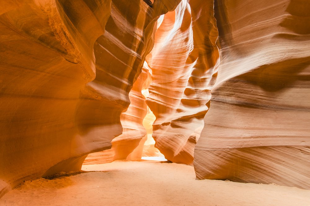 View of the famous Antelope Canyon slot canyon, striated orange rock with sandy floor with brilliant colors.