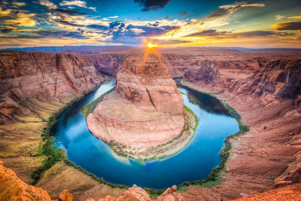 Dusk at Horseshoe Bend with epic sunset colors and a  sunburst illuminating the red rock landscape where a river bends sharply, creating a horseshoe shape.
