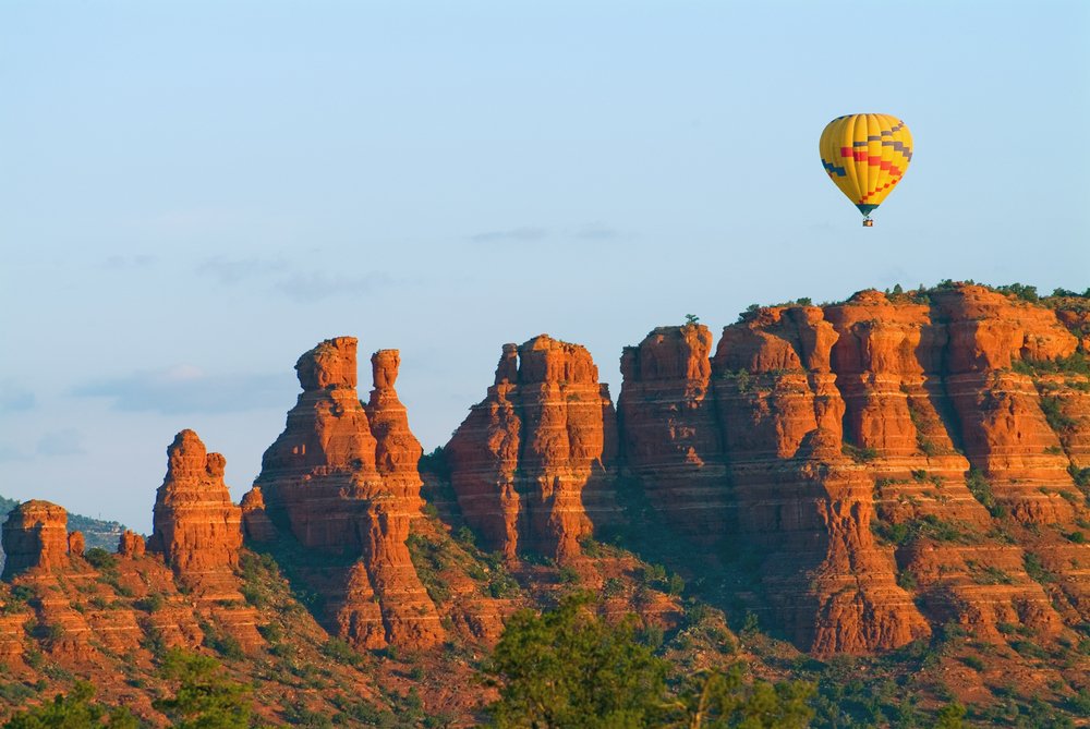 Yellow hot air balloon rising over the red rock landscape of Sedona, Arizona