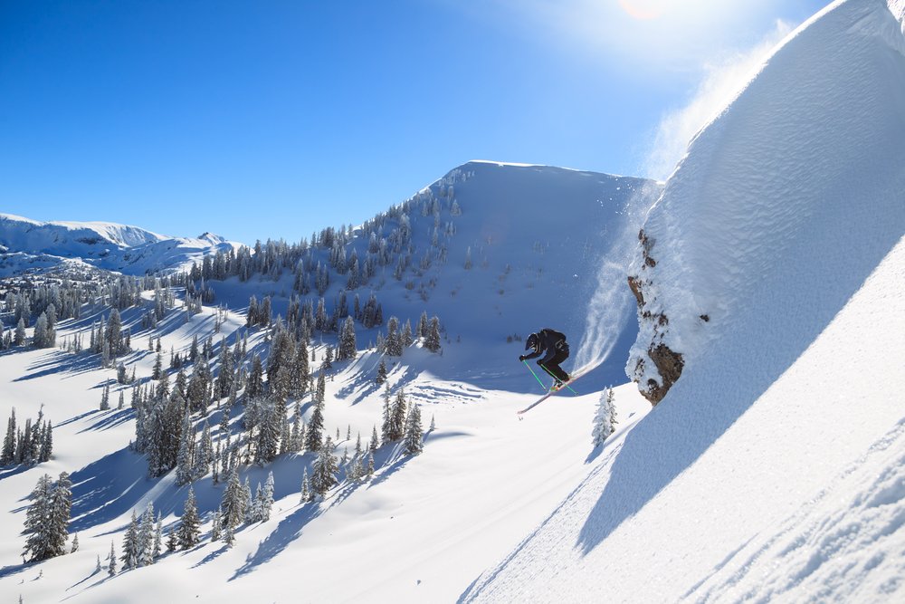 A man skiing doing a large jump in the backcountry landscape of the Grand Tetons with a powder trail behind him.
