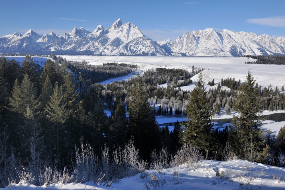 View over a winter Grand Teton landscape with a river, trees, and snow-covered mountains.