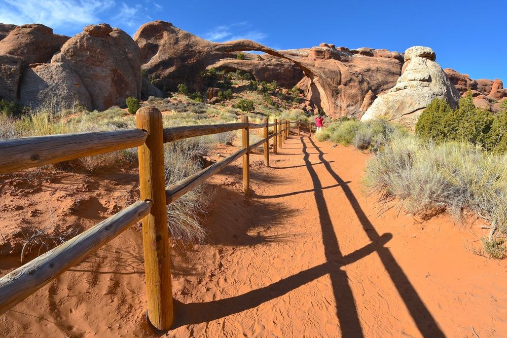 A nearly empty trail in Devils Garden in Arches National Park with red sand on the trail and views of the red rocks and arches around it.