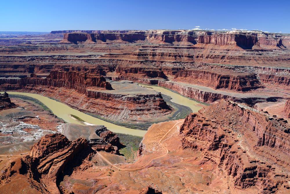 An overlook in Dead Horse Point State Park where you can see a bend in the Colorado River that has hollowed out a canyon, with red rocks in layers on the sides of the canyon.