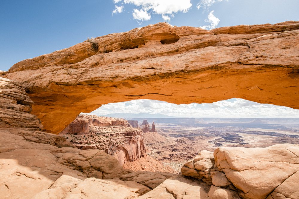 A view of Canyonlands National Park as seen through the empty space of a rock arch, Mesa Arch, looking out onto the landscape.