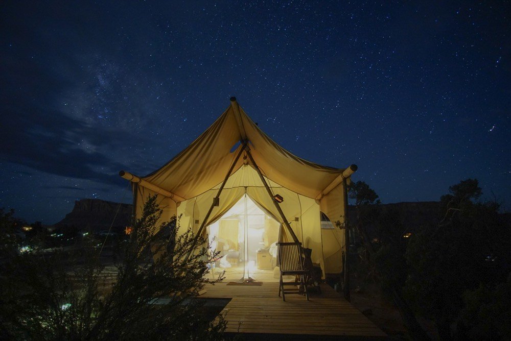 Glamping tent lit up from within with starry sky behind it