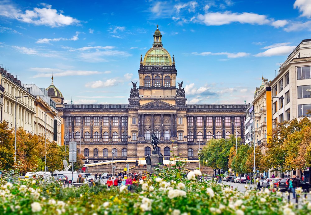 The National Gallery building with a green dome on the rooftop and sculptures on either side, flowers in the foreground of the photo.