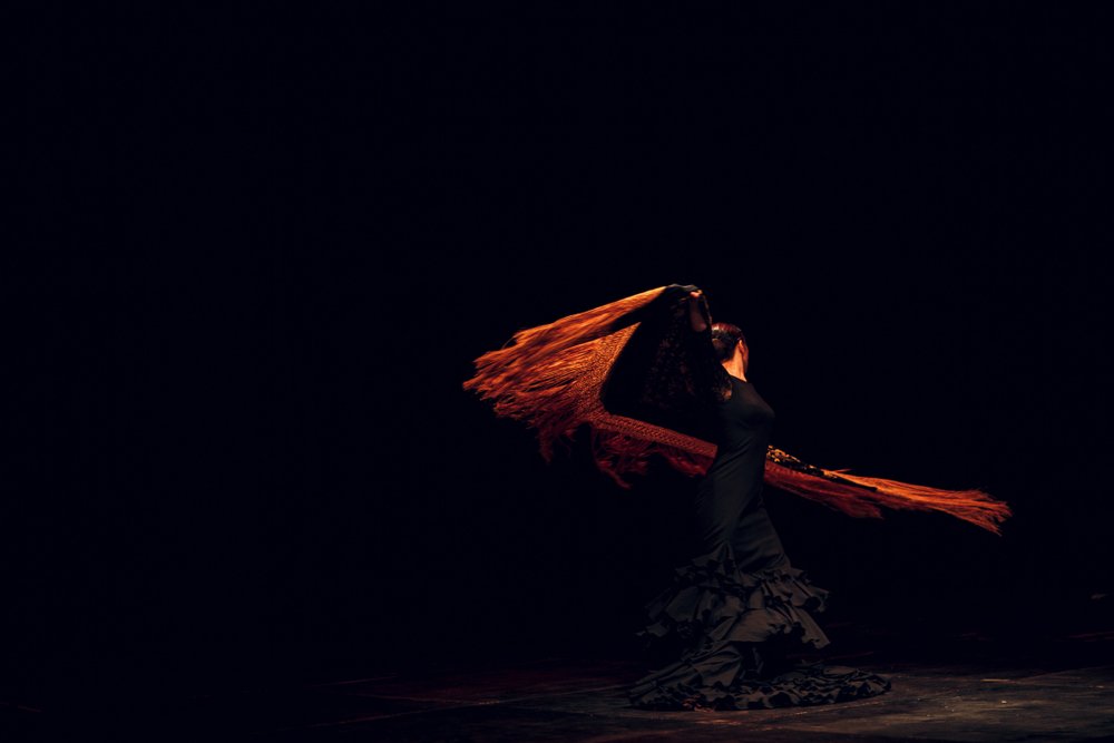 A female flamenco dancer in a dark room swirling her scarf around artistically.