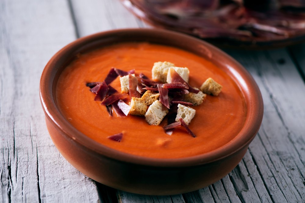 A bowl of red soup topped with meat and croutons at a Spanish restaurant.