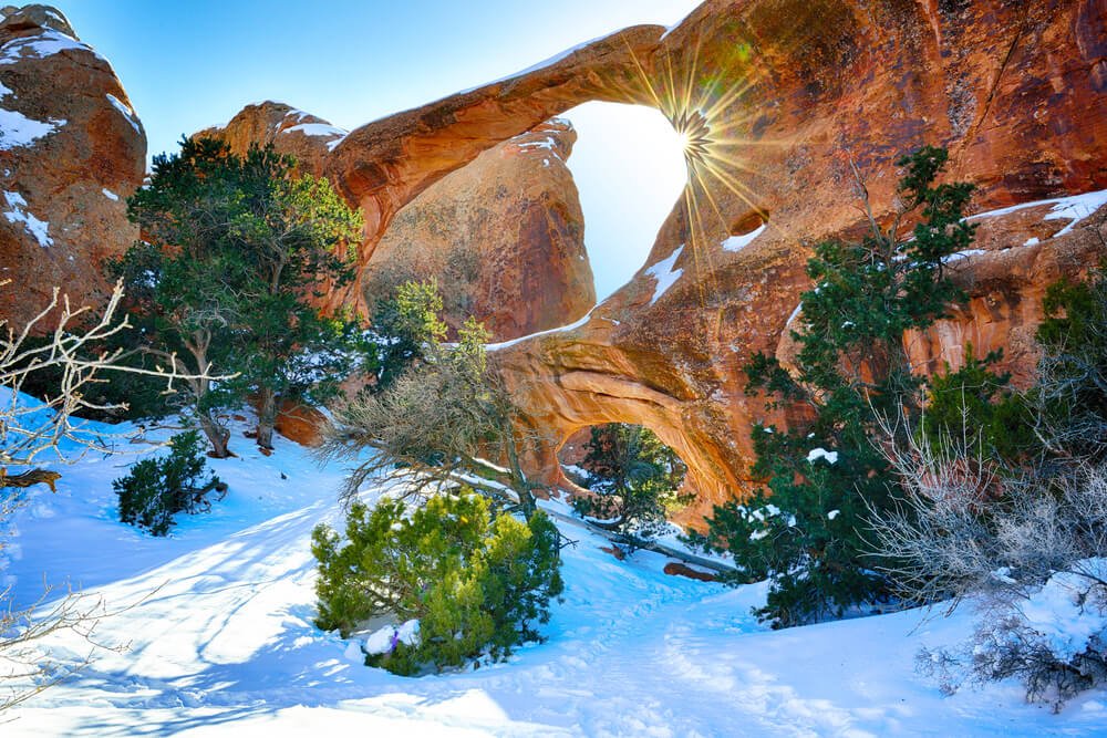 The famous Double O Arch in winter, two arches one on top of the other in the winter snow with a sunburst coming through the top arch.