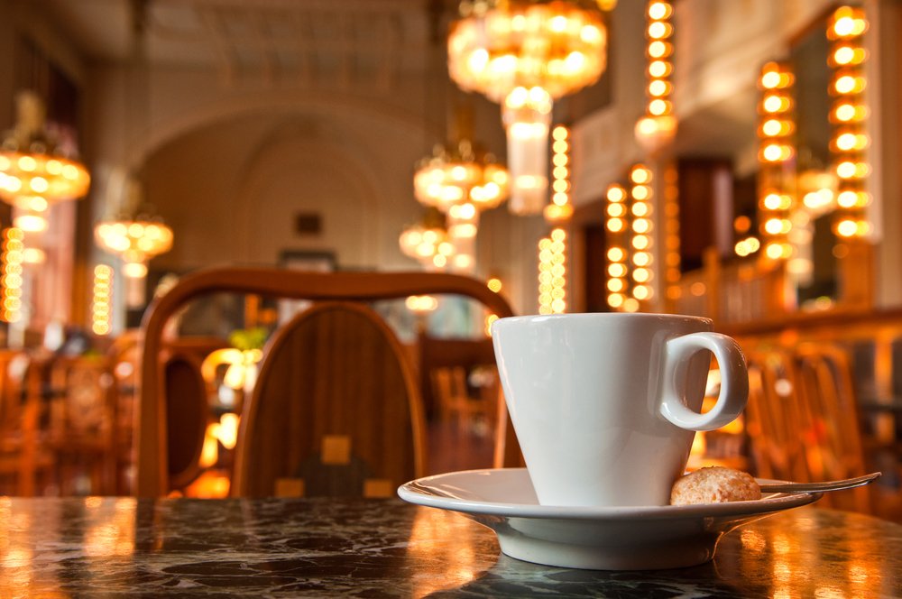 Cup of coffee in a cafe with lit up chandeliers and other lighting in background.