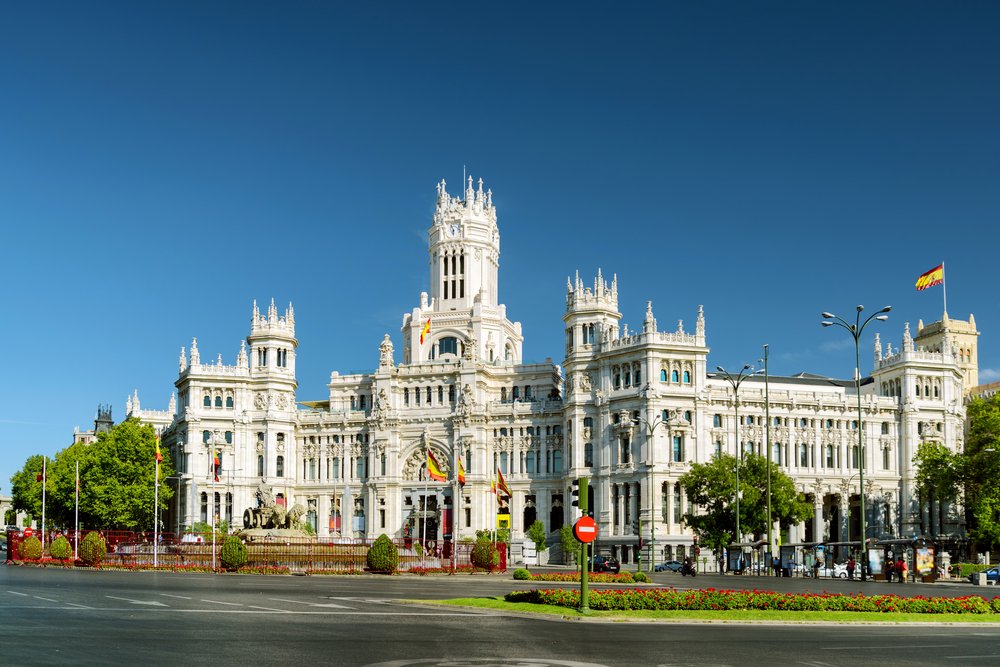 Ornate white palace with a Spain flag and an empty road in front of it