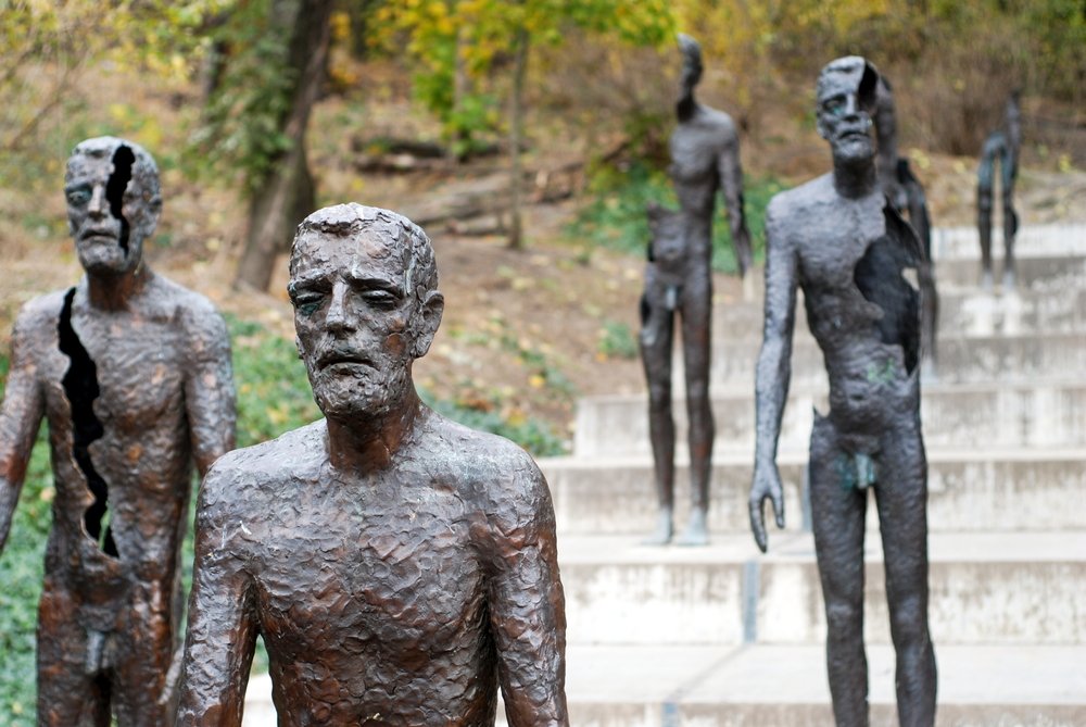 Sculptures of men on a set of stairs, the men appear to be torn or decaying with pieces missing from the sculptures