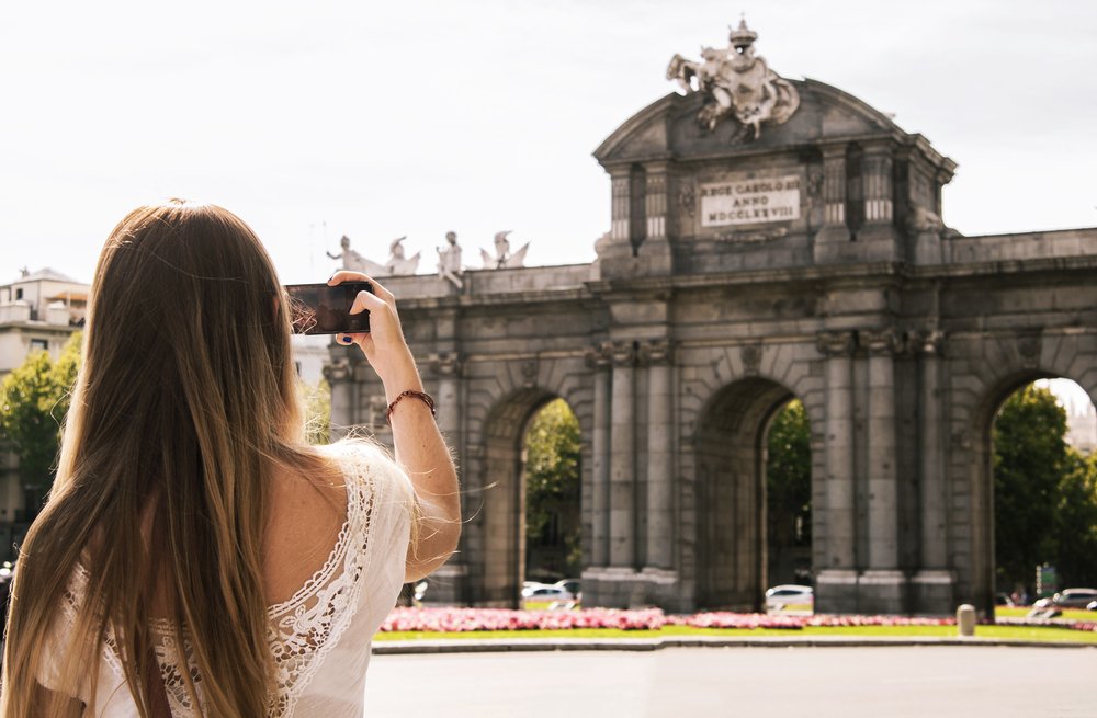 A light-haired woman with a smartphone taking a photo of a famous Madrid landmark.