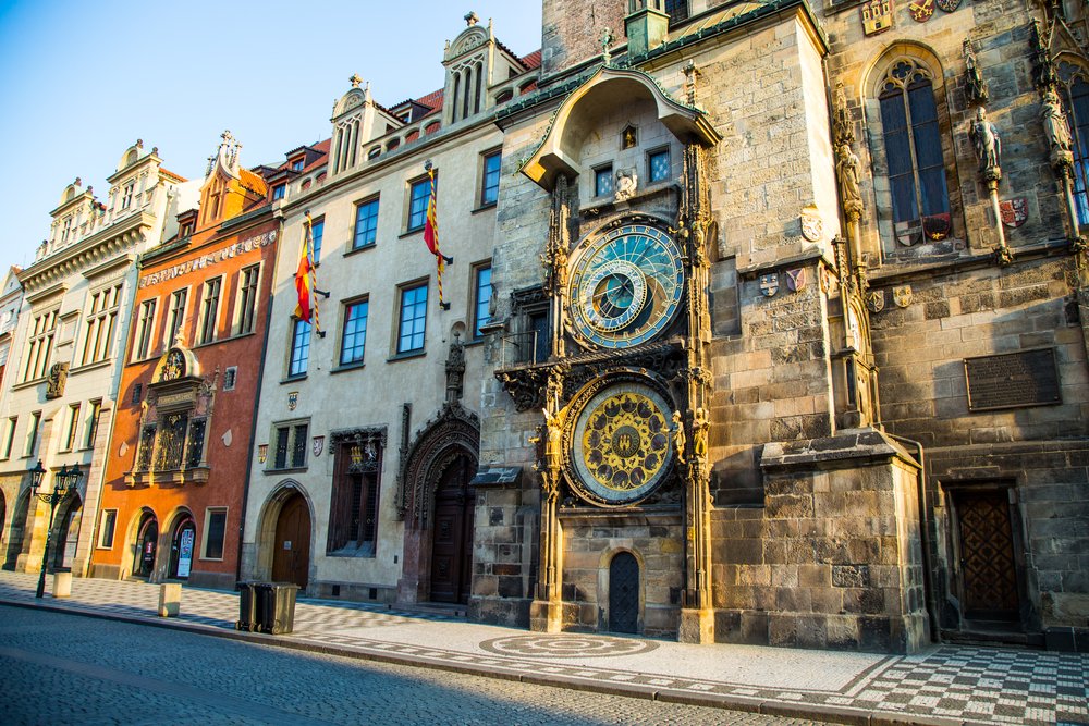 Astronomical clock in Prague surrounded by other old buildings with afternoon light shining on it.