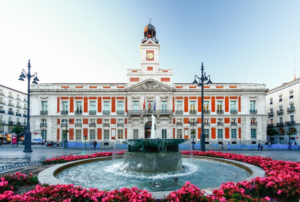 Symmetical red building with a fountain in the center and pink flowers