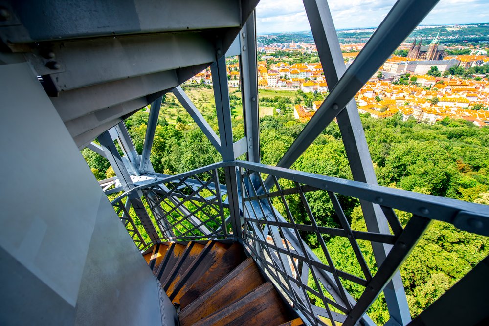 View of Prague park and distinctive red tiled roofs from the double-helix staircase of Petrin Tower, between the steel geometrical bars.