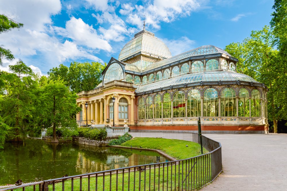 A building with clear glass walls and yellow details next to a lake on a sunny day