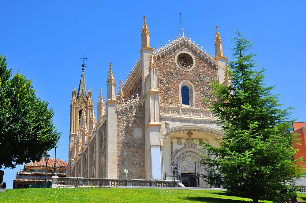 A stone and brick church with a tree in front and a grassy hill