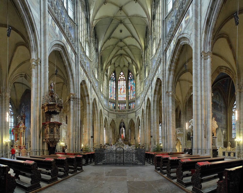 The interior of a cathedral with stained glass and high arch ceilings with rows of pews
