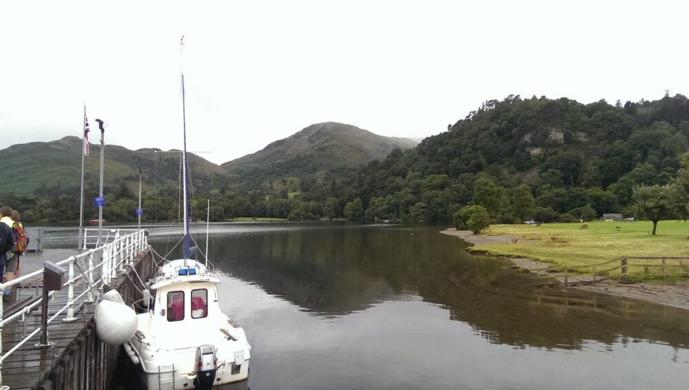 A jetty point where you can disembark from the steamboat, with a white smaller boat visible, and some hills on the lake in the distance.