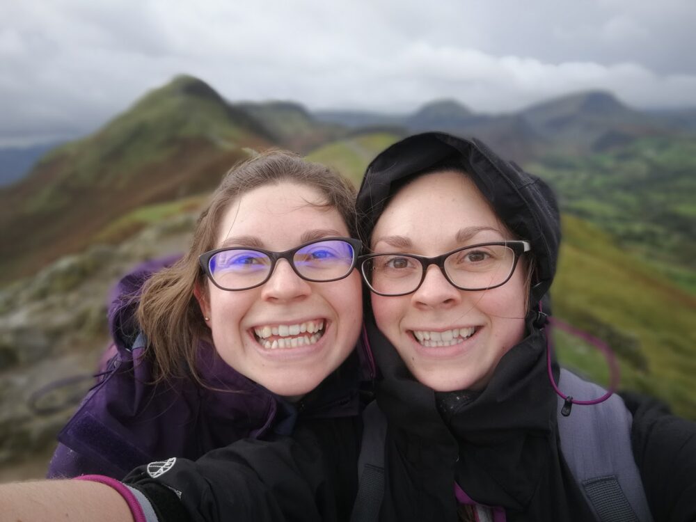 Two women, Hazel and Zoe, smiling and wearing glasses while visiting the Lake District of UK.