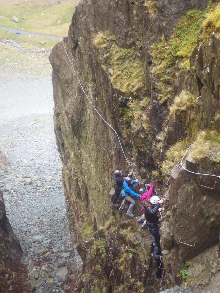 A group of four people climbing on iron ladders and railings (via ferrata) in order to ascend a cliff