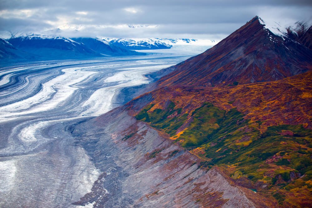 Ice fields in Canada surrounded by tall mountains covered in green and orange foliage and grass.